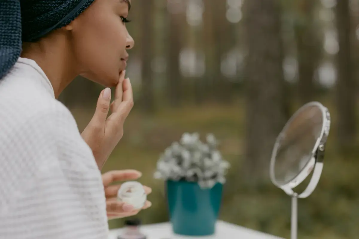 Femme qui applique une crème nourrissante près d’un miroir, en extérieur